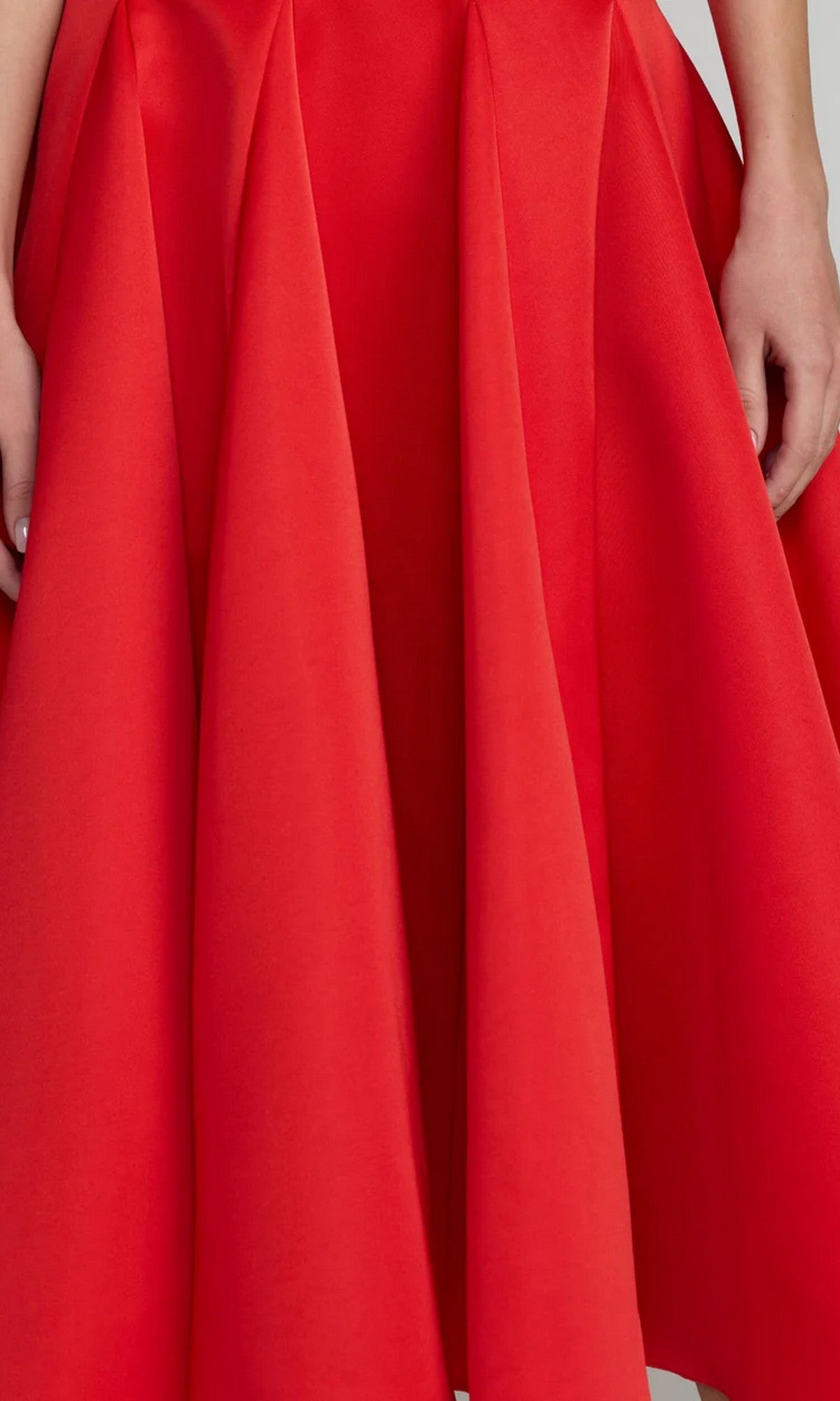 A person wearing the Mac Duggal 2364 Midi Party Dress in vibrant red—a pleated, knee-length design that captures the elegant charm of a satin party dress; only the lower torso and hands are visible.